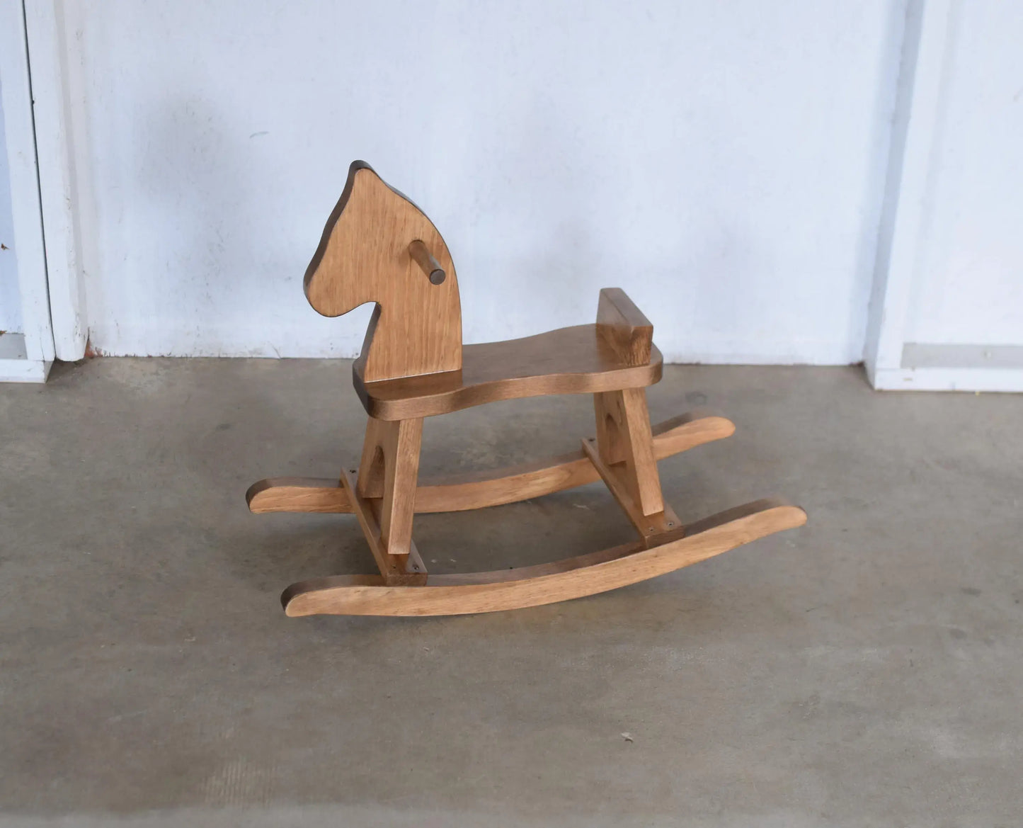 Wooden rocking horse on a concrete floor with a white wall background