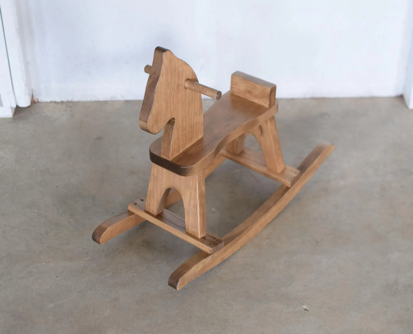 Wooden rocking horse on a concrete floor with a white wall background