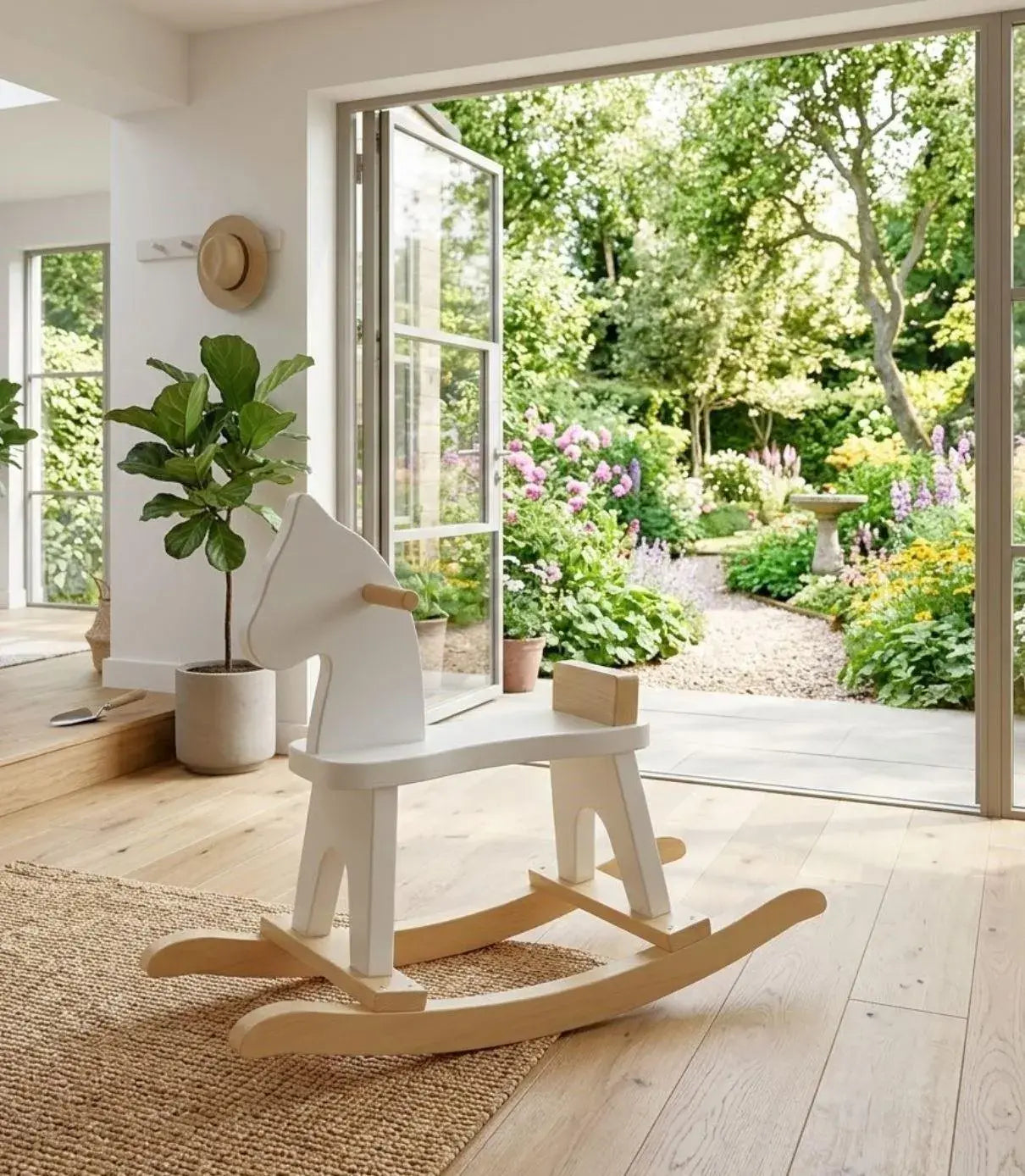 White rocking horse on a wooden floor with a garden view through a glass door.