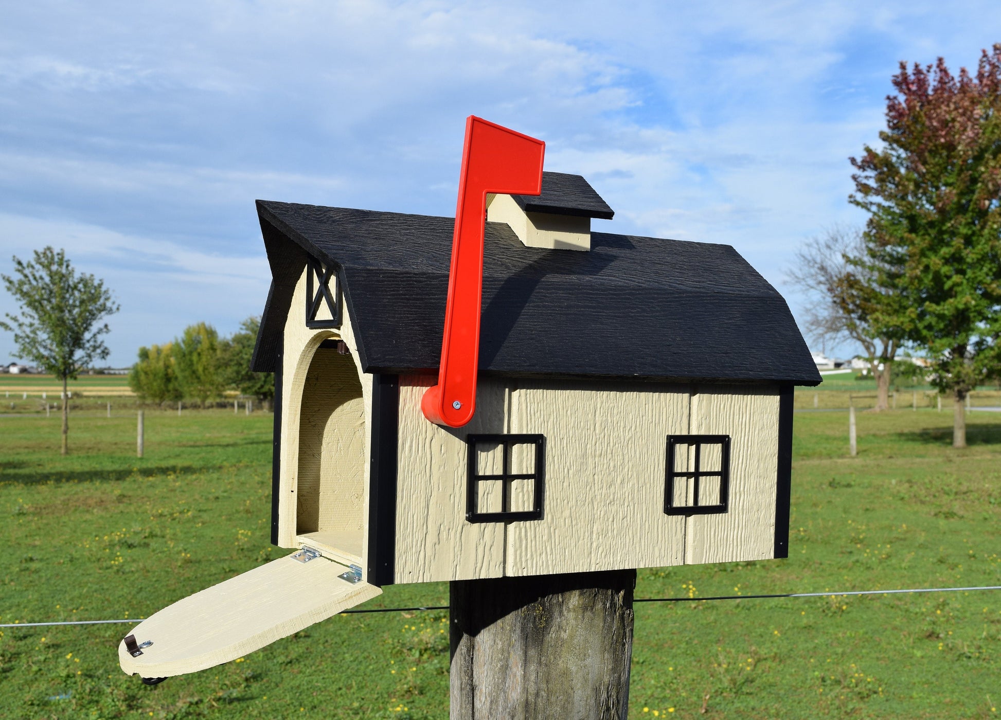 beige and black barn mailbox with red flag and open door